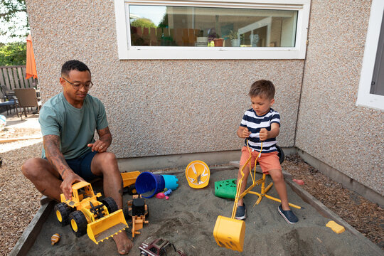 Father and son playing with toy diggers in sandbox, candid momen