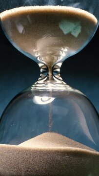 Concept of turning back time. Hourglass with grains of sand on a dark background. Shot on super slow motion camera 1000 fps.