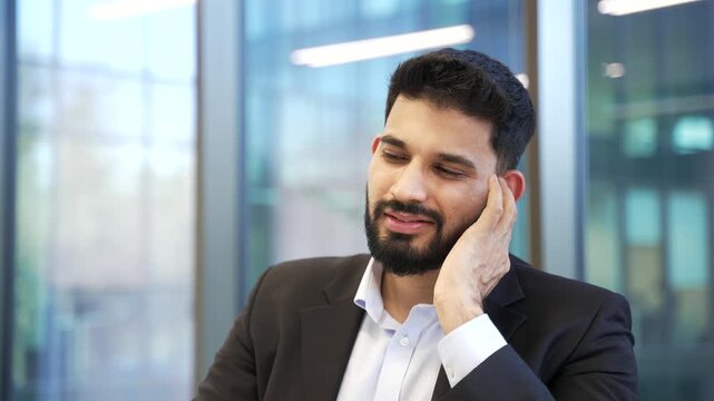 Sick businessman in suit suffers from ear pain sitting in office. Unhealthy male touches his ear with his fingers, has furuncle, eczema, shingles ear diseases or otitis media. Earache. Close up