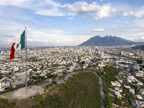Aerial view of the large Mexican flag on a tall pole overlooking the urban cityscape of Monterrey with the Cerro de la Silla mountain in the background, Monterrey, Nuevo Leon, Mexico.