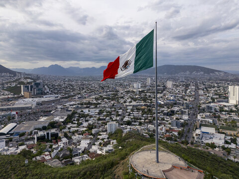 Aerial view of the large Mexican flag waving atop the Monumento a la Bandera overlooking the sprawling urban landscape and mountains of Monterrey, Nuevo Leon, Mexico.