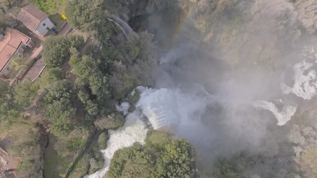 Aerial view of the powerful Marmore Falls cascading through lush green forests and rocky cliffs in Terni, Umbria, Italy.