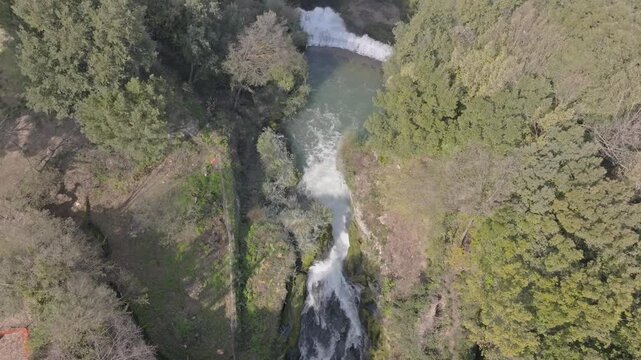 Aerial view of the cascading waters of Marmore Falls surrounded by lush green forest and rocky terrain in Terni, Umbria, Italy.