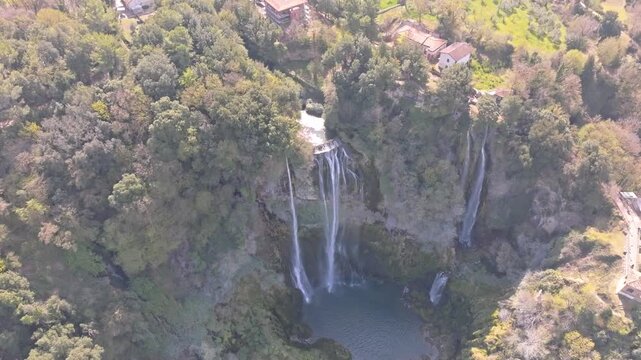 Aerial view of the cascading waters of Marmore Falls surrounded by lush green forests and rocky cliffs in Terni, Umbria, Italy.