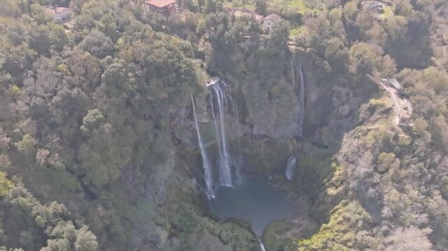 Aerial view of the cascading Marmore Falls surrounded by lush green forests and rocky cliffs in Terni, Umbria, Italy.