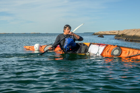 Sea kayaker practices a brace stroke with his kayak heeled on its side in morning light with copy space on Georgian Bay, Ontario, Canada