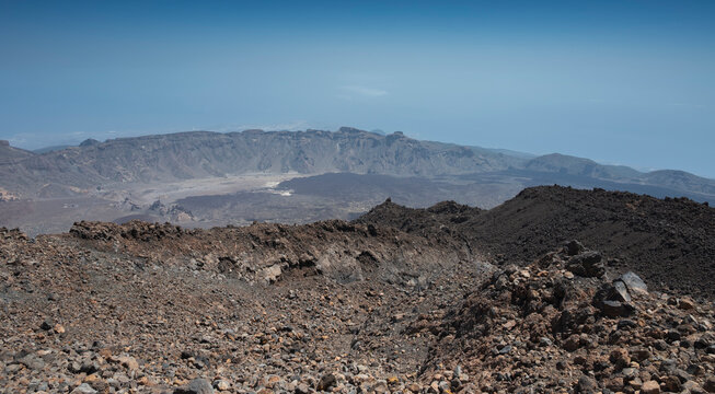 Lava flows spread across the caldera of Las Ca&ntilde;adas del Teide, Tenerife, Spain, contrasting with rugged volcanic cliffs and the arid landscape under a clear blue sky