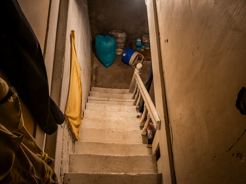 Looking down steep wooden basement stairs into a dark cellar storage space filled with old household items and clutter   