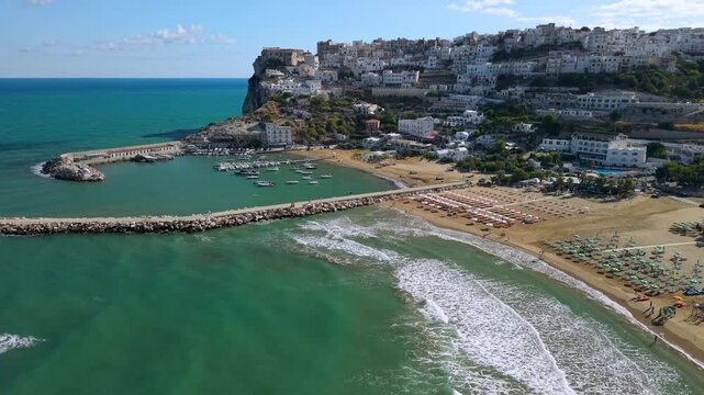 Peschici Gargano Puglia Italy 4K drone video. sea waves sounds. panning view of long beach and small marina white cascade cliff town. Travel b roll stock footage italian summer travel destination