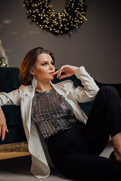 Elegant woman in festive outfit posing by a beautifully decorated Christmas wreath.