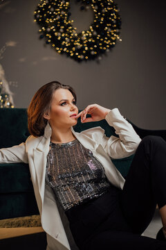 Elegant woman in a sparkling top sitting by a Christmas wreath in a stylish lounge.