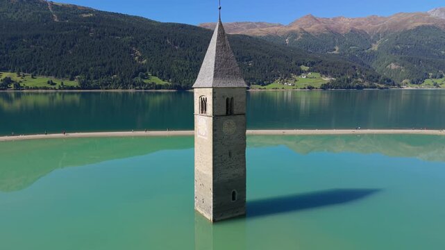 Aerial orbit around the Lake Resia bell tower in sunny South Tyrol