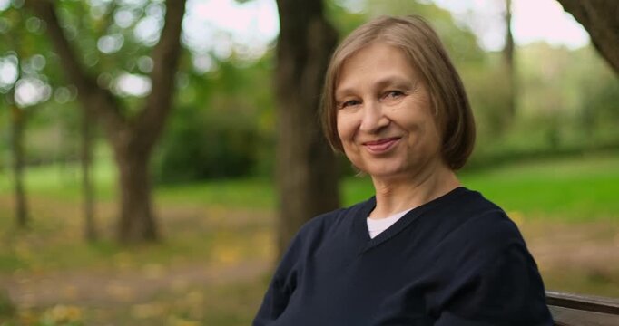 Beautiful smiling mature blond woman sitting on the bench in park