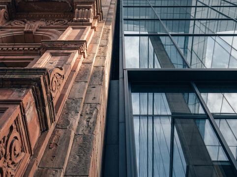 Ornate historic red sandstone building facade contrasts with a modern glass and steel skyscraper in an urban cityscape
