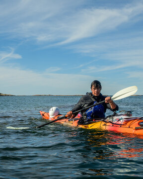 Vertical view of a sea kayaker in an orange kayak paddling under a streaked blue sky with copy space on Georgian Bay, Ontario, Canada