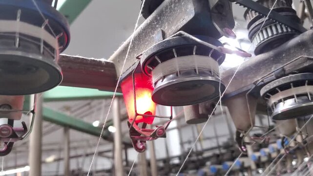 Red alert light on circular knitting machine in textile factory
A circular knitting machine in a textile factory displaying a flashing red warning light indicating a yarn break or machine fault. The a