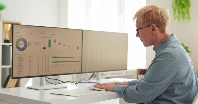Senior woman analyst reviews finance dashboard data. She works at a computer, monitoring cash flow, expenses and budgets in a bright office. Supports informed financial business decisions.