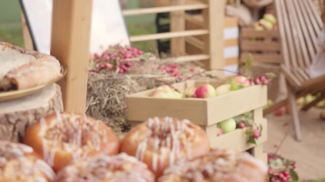 Blurred sweet baked pastries fill foreground while camera focus shifts to fresh raw ingredients. Wooden crate holds ripe apples on hay highlighting integrated farm production process.