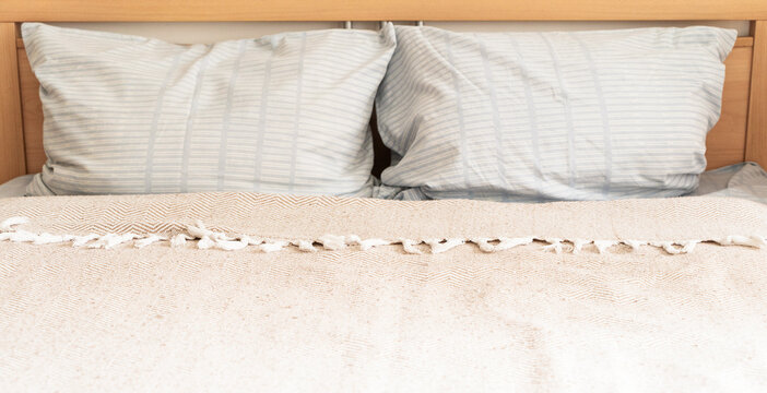 Cozy bedroom, wooden headboard, light blue striped pillows, textured throw with fringe. Slow Living philosophy, conscious consumption