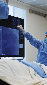 Cardiologist pointing at coronary angiogram on monitor during cardiac catheterization, doctor explaining X-ray image in cath lab, vertical