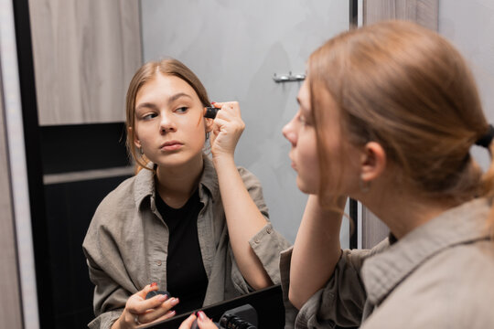 Teen girl doing her makeup while looking in mirror, beauty routine