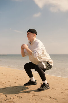 Young man doing squats on sandy sea beach before running outdoors