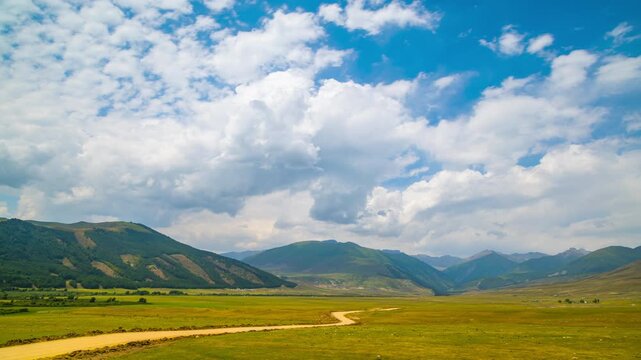 static surface-level timelapse of white clouds flowing above mountain Kyrchyn valley in Kyrgyzstan with dusty dirt road