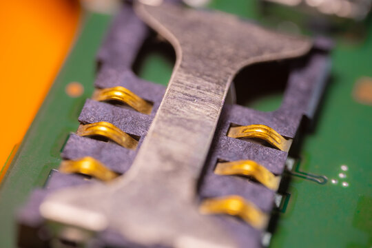 Macro view of gold electrical contacts on a green circuit board beneath a dark metal component with shallow focus and industrial electronics detail
