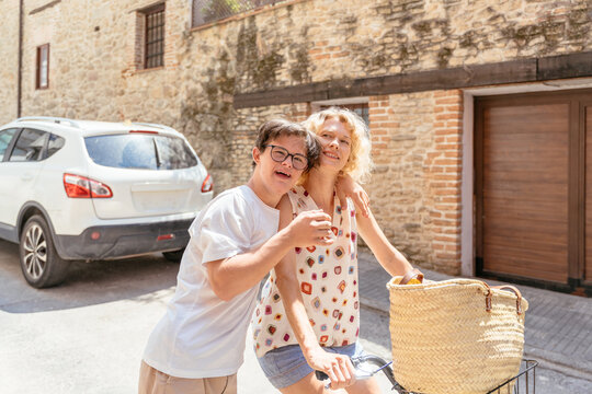 Young man with Down syndrome embracing adult woman beside tricycle on sunny street in Spain