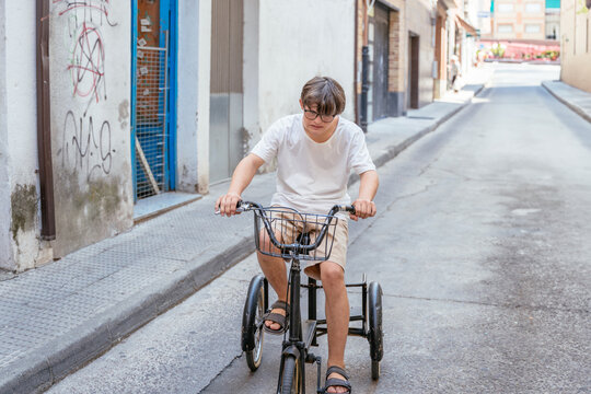 Young man with Down syndrome riding adult tricycle alone through street in Spanish town