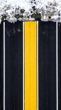 Yellow Road Marking with Snow Accumulation on Top of Asphalt Lane
