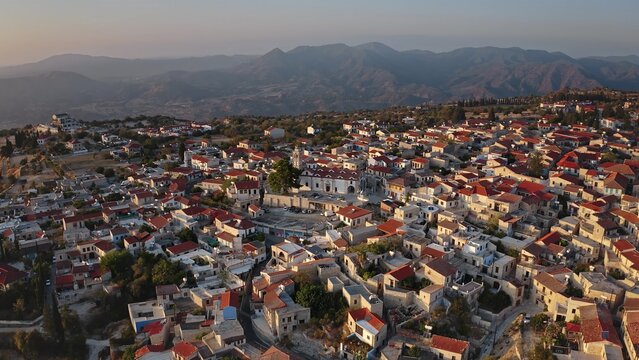Aerial view of the village of Omodos with its traditional stone houses, red-tiled roofs, and central church square nestled against the Troodos mountains in Omodos, Cyprus.