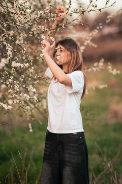 Cheerful teenage girl fooling around outdoors near a flowering tree, vintage retro photograph with strong film grain and noise