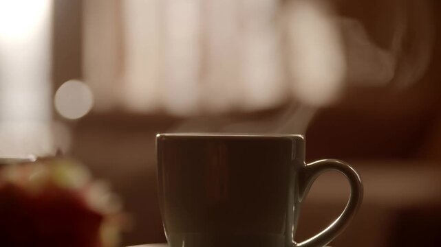 Slow motion static close up of steaming coffee mug on table in cozy kitchen morning light