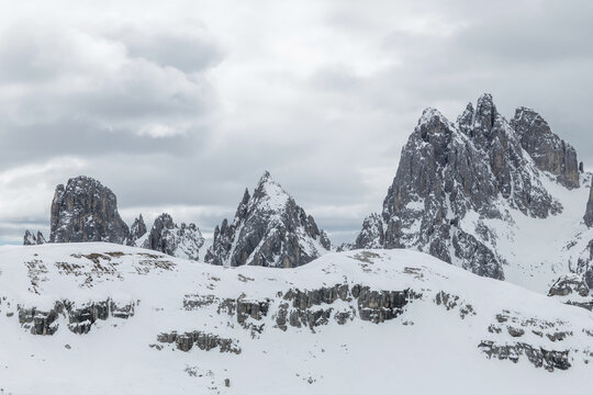 Snow covers the mountain peaks in the Dolomites, Italy. This winter scenery shows Tre Cime and alpine areas under a cloudy sky.