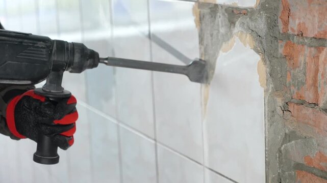 Worker use demolition hammer drill to break up tiles from wall surface. Builder with a puncher dismantles old tiles from a concrete wall. Worker remove, demolish old tiles a bathroom with jackhammer
