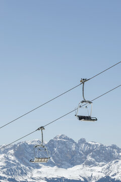 Ski lifts move over a snowy landscape in the Dolomites, Italy during winter skiing season. The mountain scenery shows the Italian Alps.