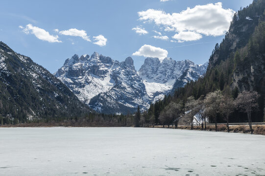 Beautiful winter landscape shows snowy peaks around Lake Landro in Dolomites Italy. The lake is frozen, reflecting the mountains above.