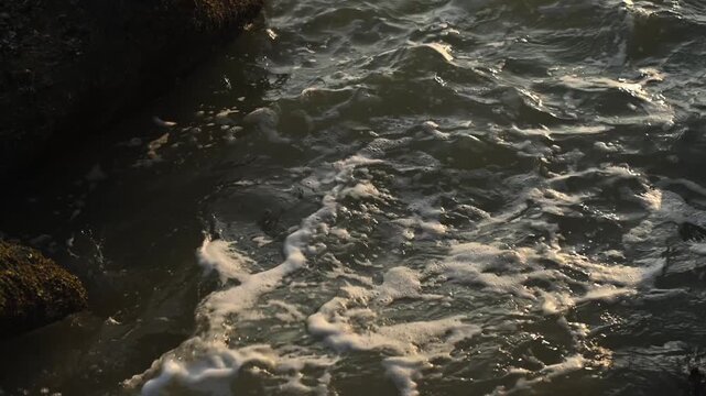 Ocean waves crashing over barnacle covered rocky shoreline with white sea foam in dramatic low light