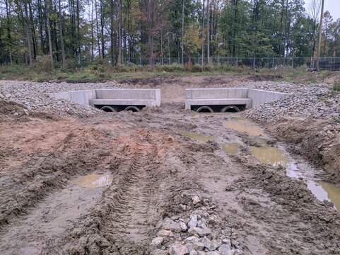 Drainage pipes set into concrete headwalls at a muddy construction site with waterlogged soil for civil engineering and flood control