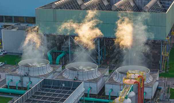 Aerial view of cooling towers and heavy industrial infrastructure releasing steam at a large manufacturing and metal processing facility in Brescia, Lombardy, Italy.