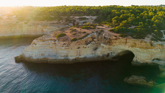 Picturesque coastal landscape of rugged limestone cliffs and clear turquoise water. Rocky cape over sea bay with stony shore under sunlight. Algarve, Portugal