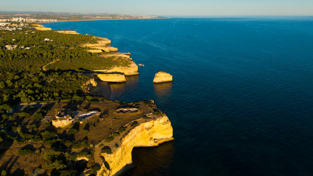 Picturesque coastal landscape of rugged limestone cliffs and clear turquoise water. Rocky cape over sea bay with stony shore under sunlight. Algarve, Portugal