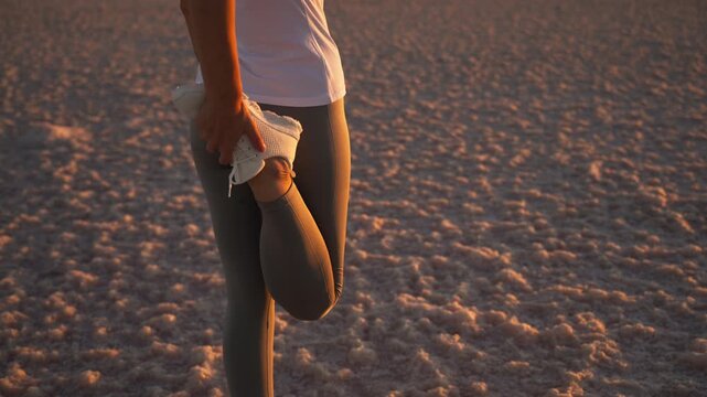Female athlete warming up her quadriceps and stretching her legs in an outdoor landscape before running or endurance training, preparing her muscles for physical activity