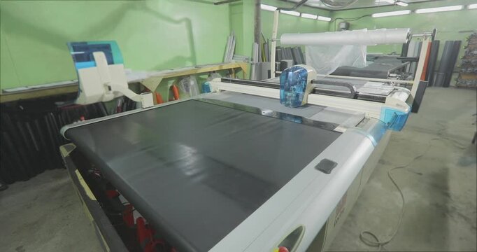 CNC Fabric Cutting Machine in Industrial Workshop. Automated cutting of grey upholstery fabric on a CNC plotter. Fabric cutting process on a CNC machine in a modern production workshop. 