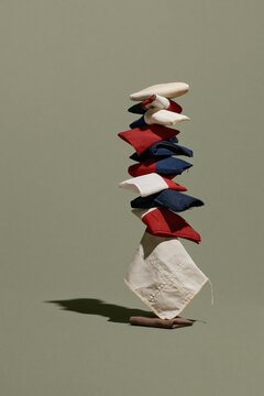 Vertical tower of folded national flags balanced in precarious equilibrium on a pale grey-green surface with copy space for international relations