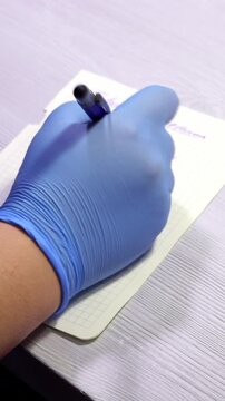 Vertical close-up shot of a doctor in blue gloves writing a prescription on paper in a clinic. Healthcare and medical consultation concept