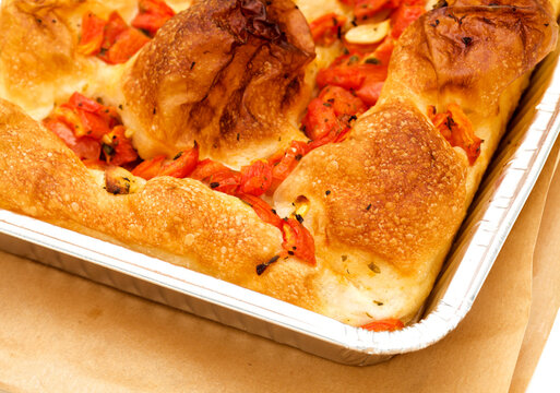 Freshly baked Italian focaccia bread with tomatoes in an aluminum tray isolated on white background
