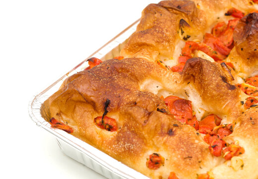 Freshly baked Italian focaccia bread with tomatoes in an aluminum tray isolated on white background
