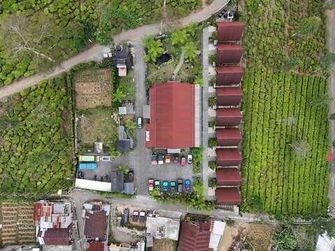 Aerial view of Kebun Teh Panama resort featuring red-roofed buildings and a parking area surrounded by lush green tea plantations in Kecamatan Garung, Jawa Tengah, Indonesia.